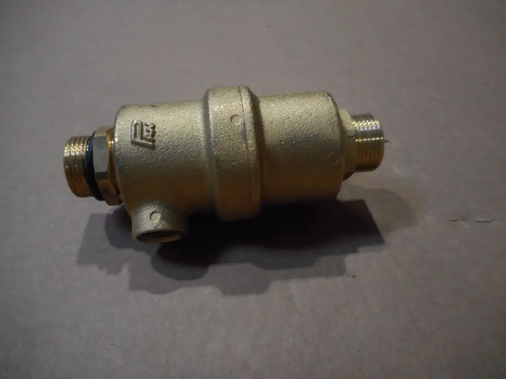 Remeha Airstop, ein zylindrisches Bauteil mit Gewindeanschlüssen, aus Metall mit goldfarbener Oberfläche, auf einem braunen Untergrund abgebildet.